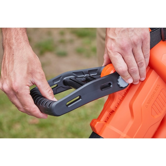 Close-up of hands adjusting BLACKDECKER BCBLV3625L1 orange leaf blower handle outdoors.