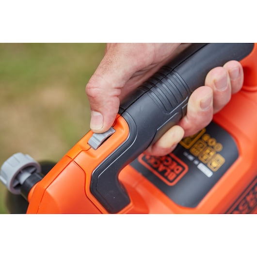 Close-up of hand operating BLACK+DECKER BCBLV36B garden blower switch, orange and black handle visible.