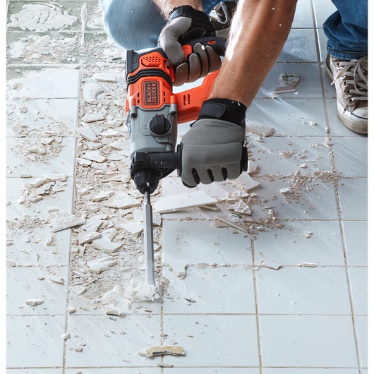 Photo of BLACK+DECKER BCD900E2K rotary hammer in use removing tiles from a white tiled floor.