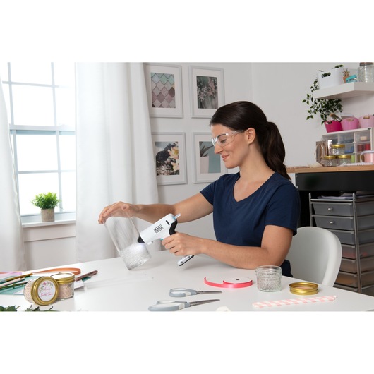 BLACKDECKER BCGL115 glue gun used on a glass jar in a craft workspace, surrounded by craft supplies.