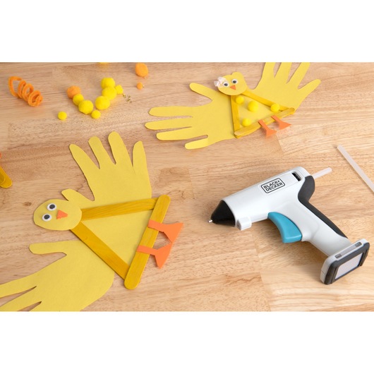 BLACKDECKER BCGL115 hot glue gun on a wooden table with yellow paper chick crafts and crafting materials, top view.