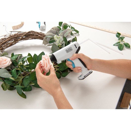 Photo of BLACKDECKER BCGL115 cordless glue gun being used to attach a pink flower to a wreath on a white table.
