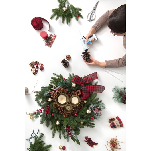 Photo of BLACKDECKER BCGL115 cordless glue gun used for creating a Christmas wreath with candles, pinecones, and ribbon.