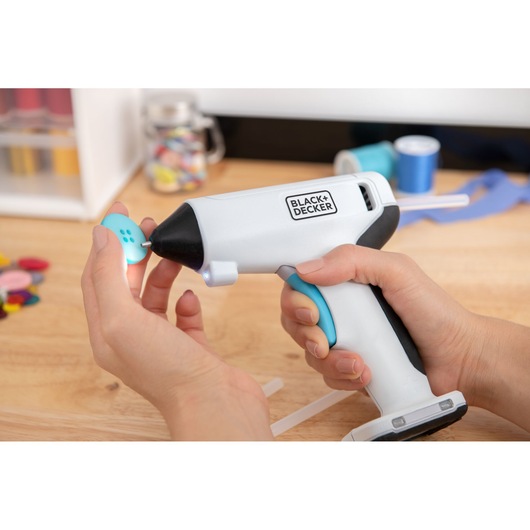 Photo of BLACK+DECKER cordless glue gun BCGL115 being used to apply glue to a blue button during a craft project.