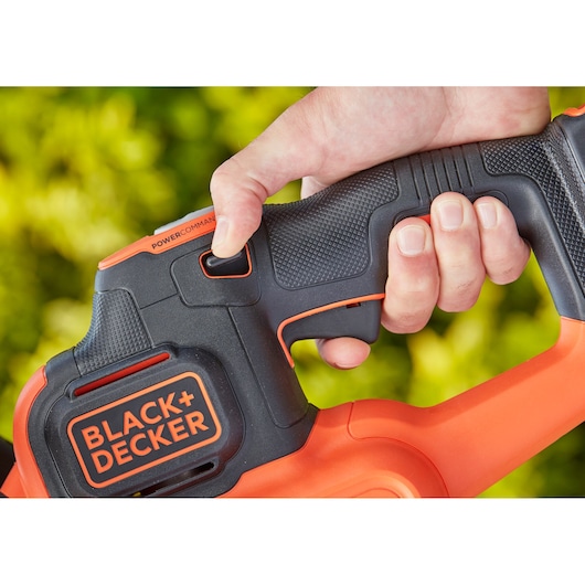 Close-up of BLACK+DECKER BCHTS36B hedge trimmer handle with hand gripping textured black and orange grip.