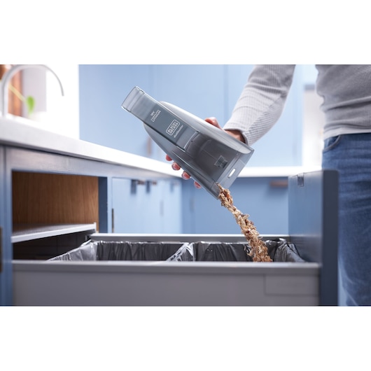 Photo of BLACK+DECKER BCHV001B handheld vacuum canister being emptied into a kitchen trash bin.