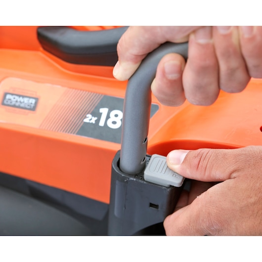 BLACKDECKER BCMW3318L2 lawn mower close-up, hand adjusting handle height with gray button, orange and black body.