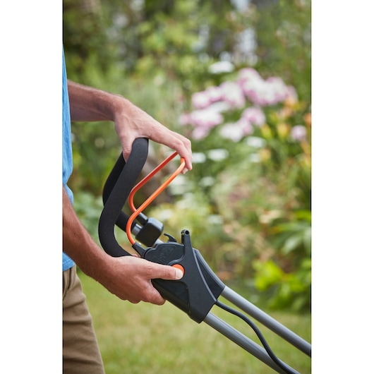 BLACKDECKER BCMW3336L2 lawn mower handle with orange accents held outdoors.