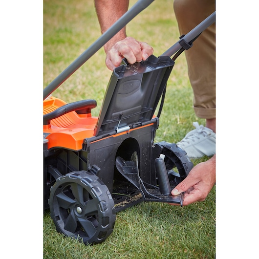 BLACKDECKER BCMW3336L2 lawn mower close-up, hands opening rear chute cover, shown on grass.