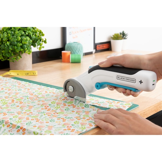 BLACKDECKER BCRC115 rotary fabric cutter, close-up use on floral patterned cloth, photography.