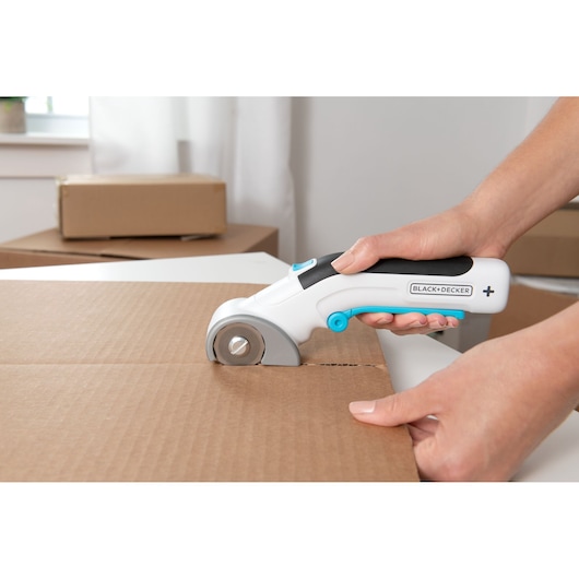 BLACK+DECKER BCRC115 electric rotary cutter trimming cardboard box, close-up of tool in use.