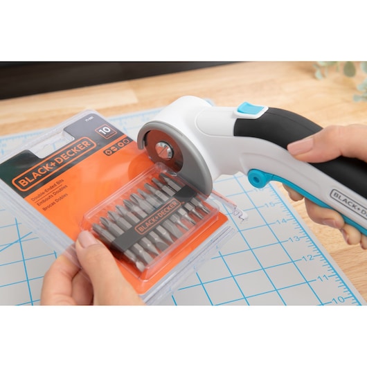 Photo of BLACK+DECKER BCRC115 rotary cutter opening an orange BLACK+DECKER double-ended bits package on a cutting mat.