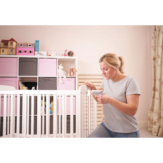 BLACKDECKER BCRTA01 handheld tool used by a woman assembling a white crib in a nursery room.