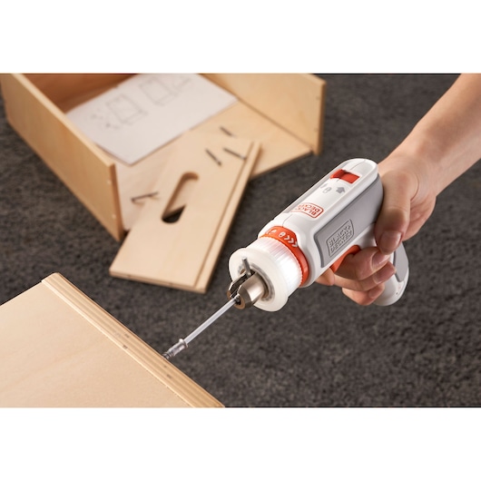 Photo of BLACK+DECKER BCRTA01 cordless screwdriver in use, assembling wooden furniture, instruction sheet visible.