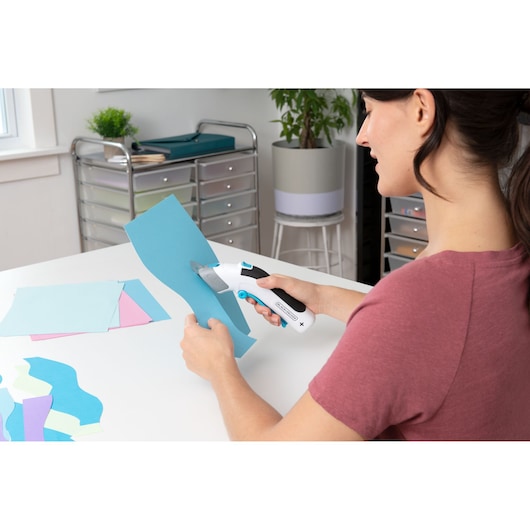 Photo of BLACKDECKER BCSC115 electric scissor cutting blue paper on a white table in a craft room.