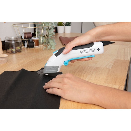 Photo of BLACK+DECKER BCSC115 electric rotary cutter being used to cut black fabric on a wooden table.