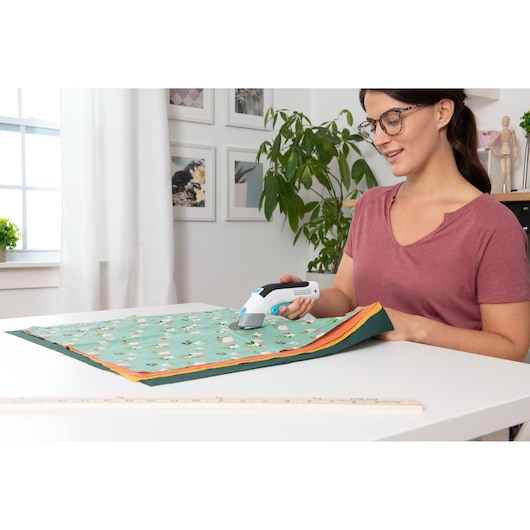 Photo of BLACKDECKER BCSC115 electric fabric scissors being used to cut patterned fabric on a table.