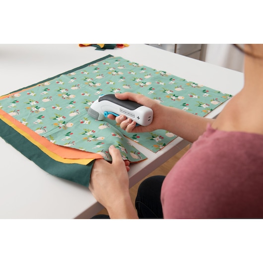 Photo of BLACKDECKER BCSC115 electric scissors being used to cut floral fabric on a white table.