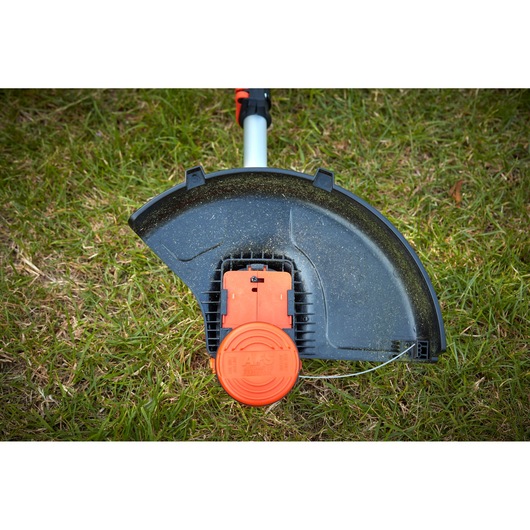 BLACKDECKER BCSTA536L1 grass trimmer head with orange line feed system, shown close-up on grass.
