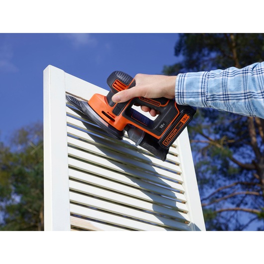 BLACKDECKER BDCDS18 cordless sander used on white shutter outdoors, orange and black tool held in hand.