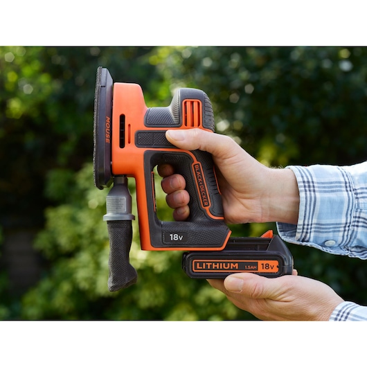 BLACK+DECKER BDCDS18 cordless detail sander held in hand, 18V lithium battery visible, orange and black finish.