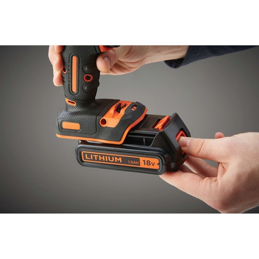 Close-up view of hands attaching an 18V 1.5Ah lithium battery to a BLACK+DECKER cordless power tool.