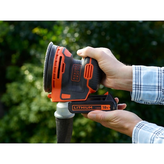 BLACKDECKER BDCROS18N cordless random orbital sander with 18V lithium battery held in hand outdoors.