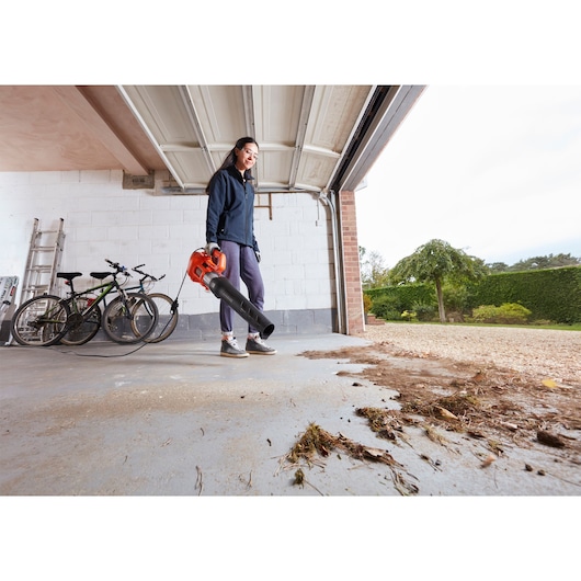 BLACKDECKER BEBL185 leaf blower in use, clearing garage floor of leaves and debris.