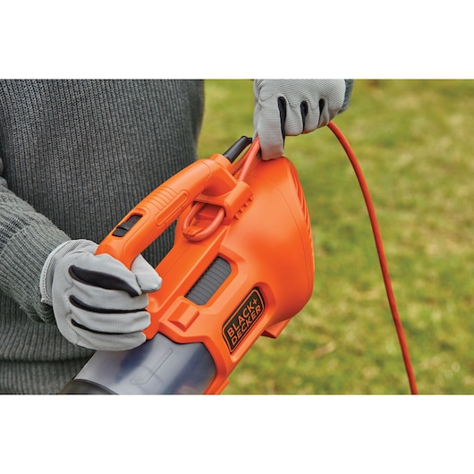 Photo of BLACK+DECKER BEBL185 orange corded leaf blower held by person wearing gray gloves outdoors.