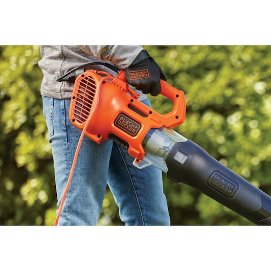 Photo of BLACK+DECKER BEBL185 orange and black corded electric leaf blower held by person wearing gloves outdoors.