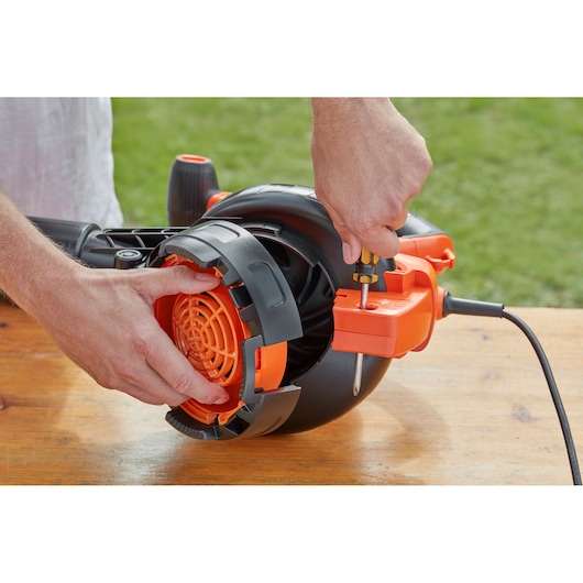 BLACKDECKER BEBLV301 leaf blower in black and orange, close-up of hands performing maintenance outdoors.