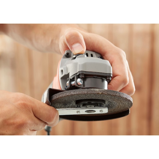 Close-up of hands adjusting BLACKDECKER BEG010 angle grinder disc, showing tool detail.