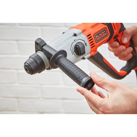 Photo of BLACK+DECKER BEHS02K rotary hammer drill with orange and black handle, shown in hand near white brick wall.