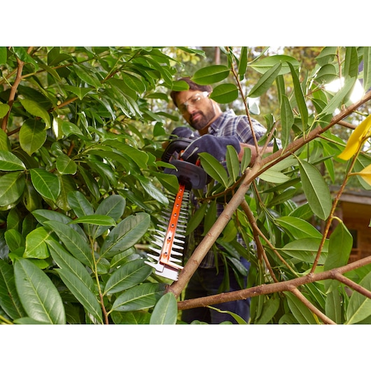 Photo of BLACKDECKER BEHTS401 hedge trimmer cutting branches in dense green foliage outdoors.