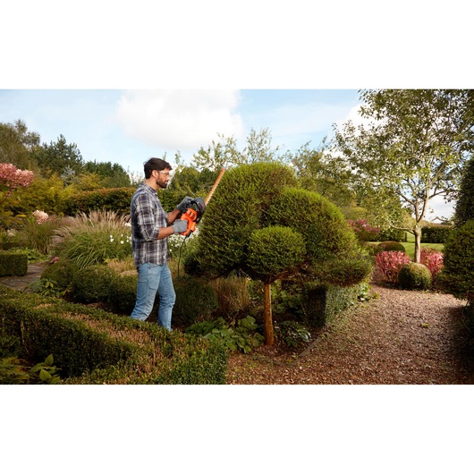 BLACKDECKER BEHTS401 hedge trimmer used outdoors, man shaping garden shrubs, orange and black tool visible.