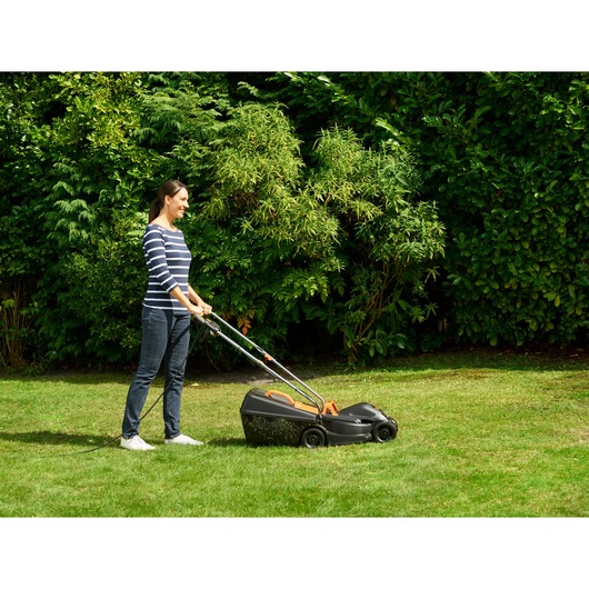 Photo of person using BLACKDECKER BEMW351 electric lawn mower on grass in a garden setting.