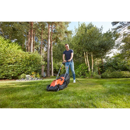 BLACKDECKER BEMW451 corded lawn mower in use on grass in a garden setting.
