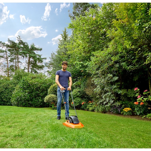 Photo of BLACKDECKER BEMWH551 orange hover mower in use on garden lawn.
