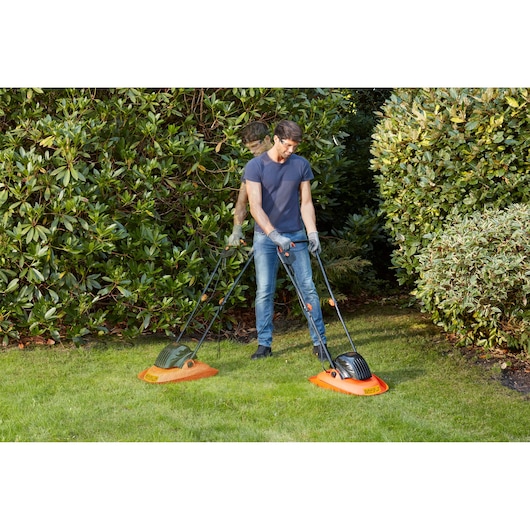 Photo of a person using a BLACK+DECKER BEMWH551 orange hover lawn mower on grass in a garden.