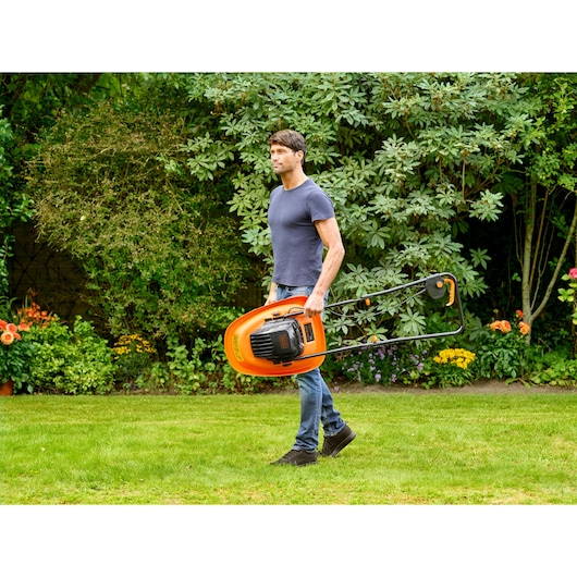 Person carrying BLACKDECKER BEMWH551 orange electric lawn mower in a garden.