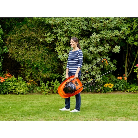 Photo of BLACKDECKER BEMWH551 orange lawn mower being carried in a garden by a person.