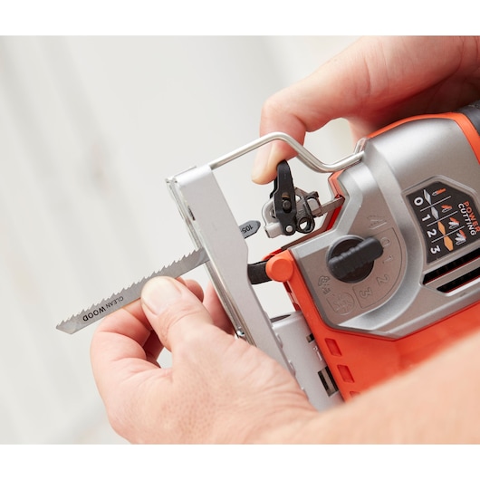 Photo of BLACKDECKER BES610K jigsaw, close-up of hands changing wood blade, showing control panel and orange housing.