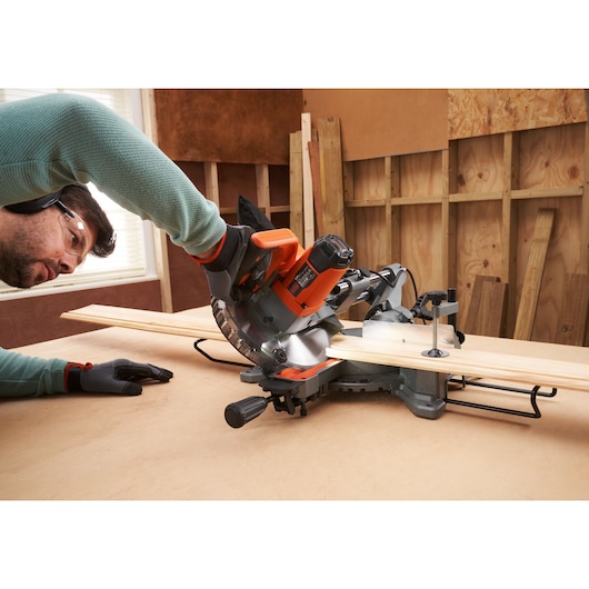 BLACKDECKER BES701 miter saw in use cutting wooden planks on a workbench in a workshop.