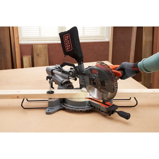 BLACK+DECKER BES701 miter saw side view cutting wood, gloved hand operating handle in workshop.