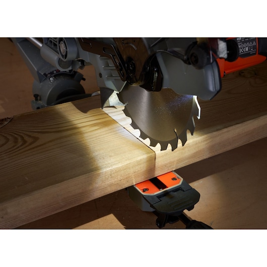 BLACKDECKER BES701 miter saw blade cutting light-colored wood plank, side view, close-up.