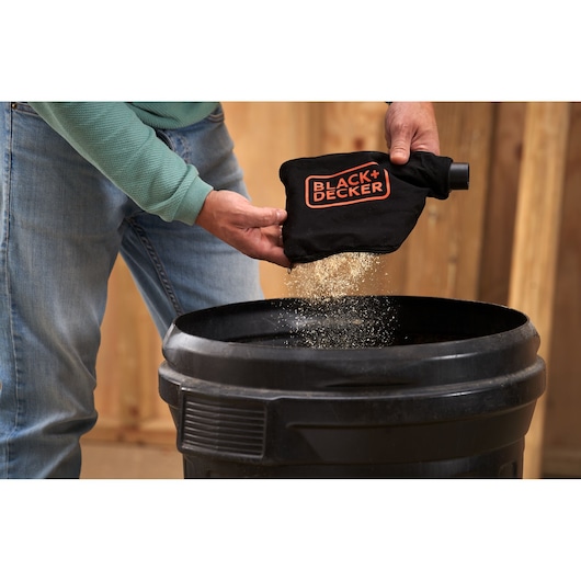 Photo of person emptying dust from BLACK+DECKER BES701 dust bag into a black container.