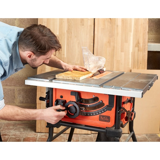 Photo of BLACK+DECKER BES720 table saw in use, orange body, clear blade guard, wood being cut.
