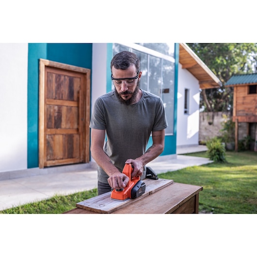 Photo of person using BLACKDECKER BEW712 electric planer on wooden plank outdoors.