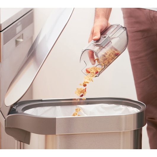 BLACKDECKER BHFEA515J vacuum dustbin being emptied into a stainless steel trash can, close-up side view.