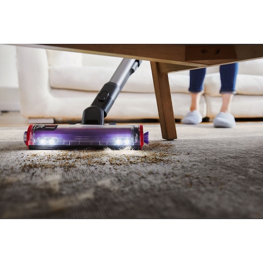 BLACKDECKER BHFEA640WG cordless vacuum cleaning carpet under table, close-up with LED lights visible.